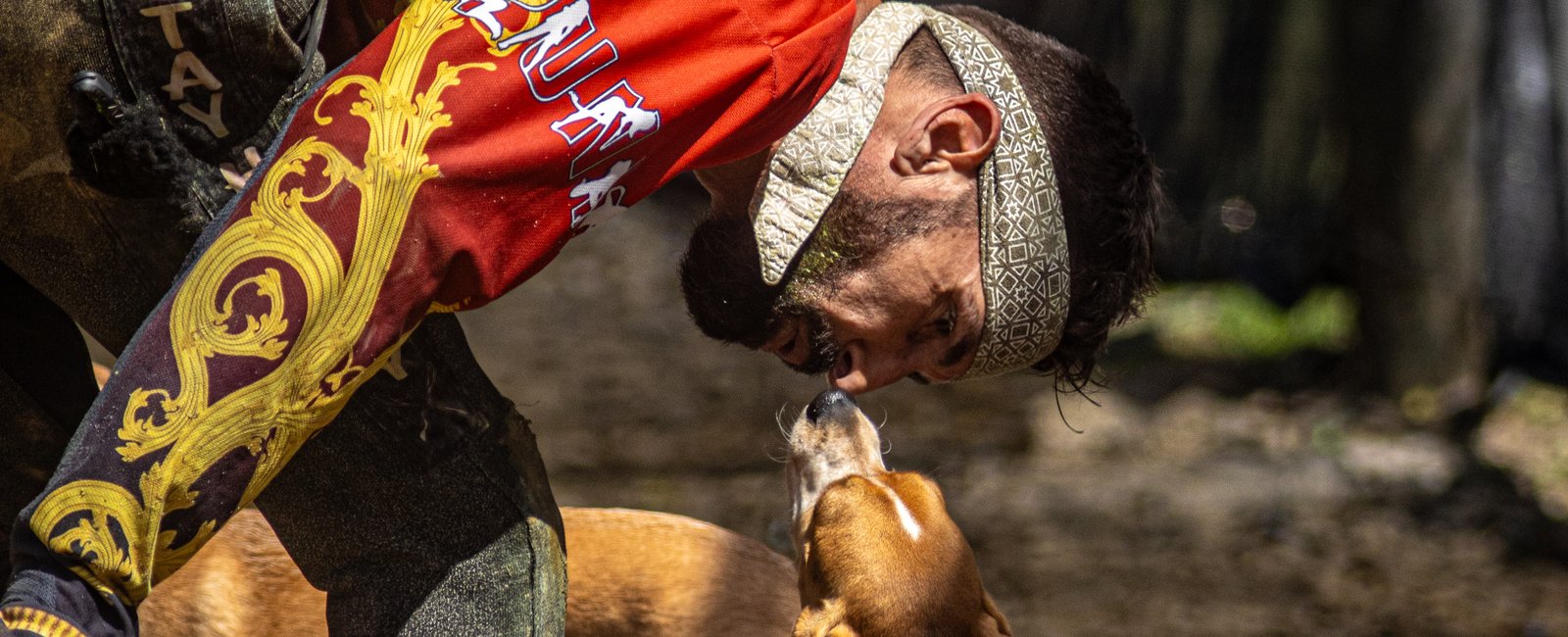 A muddy player bent down getting a kiss from the field beagle in the pits